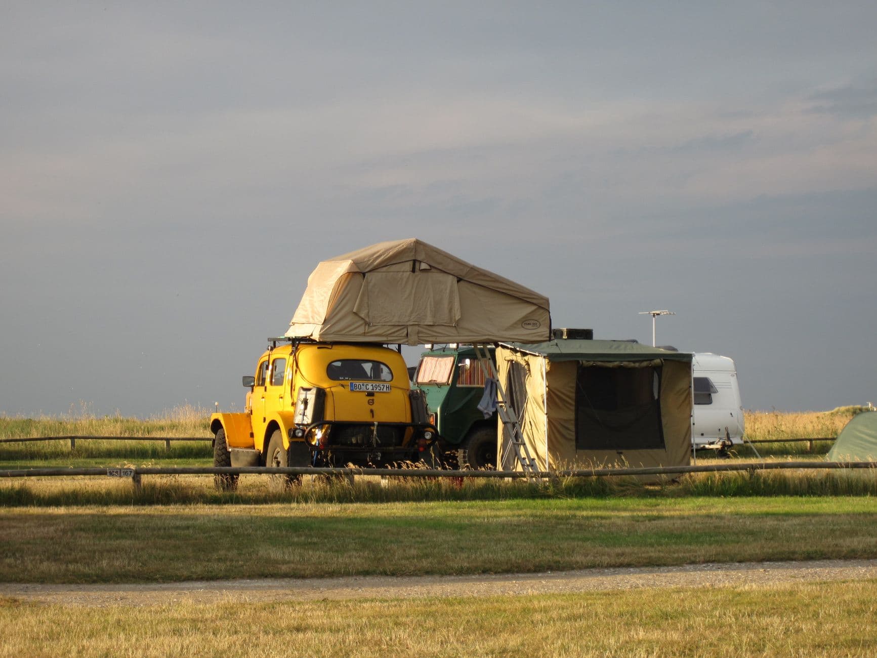 Outdoor camping scene with a classic car, roof tent, and field backdrop, ideal for travel enthusiasts.