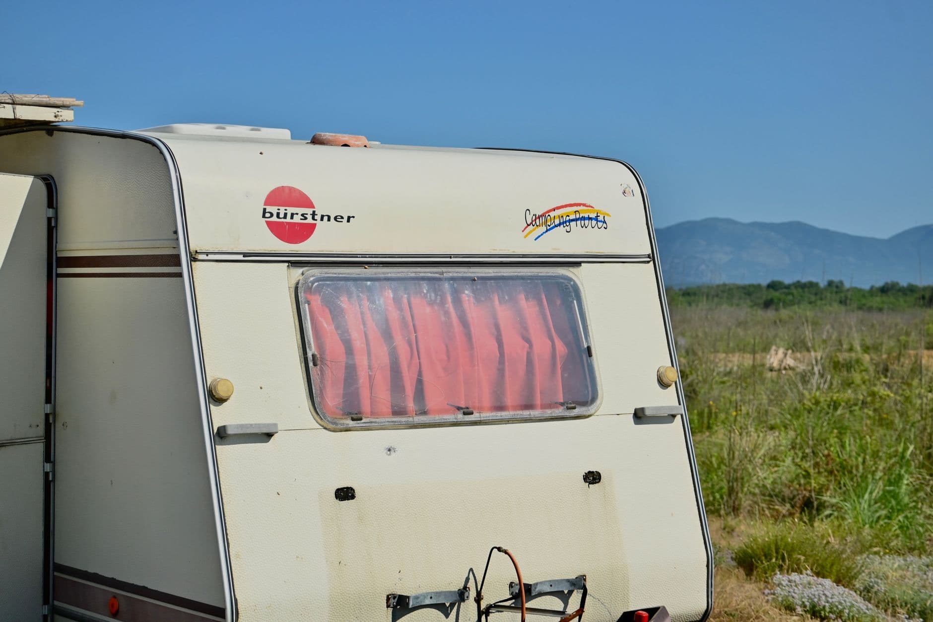 Un camping-car Bürstner vintage dans un cadre extérieur pittoresque avec montagnes et campagne.
