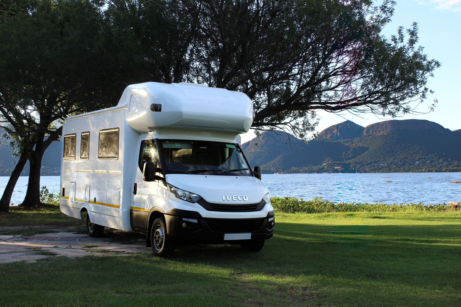 Un camping-car moderne garé près d'un lac tranquille avec des montagnes en arrière-plan, parfait pour les amateurs de voyage.