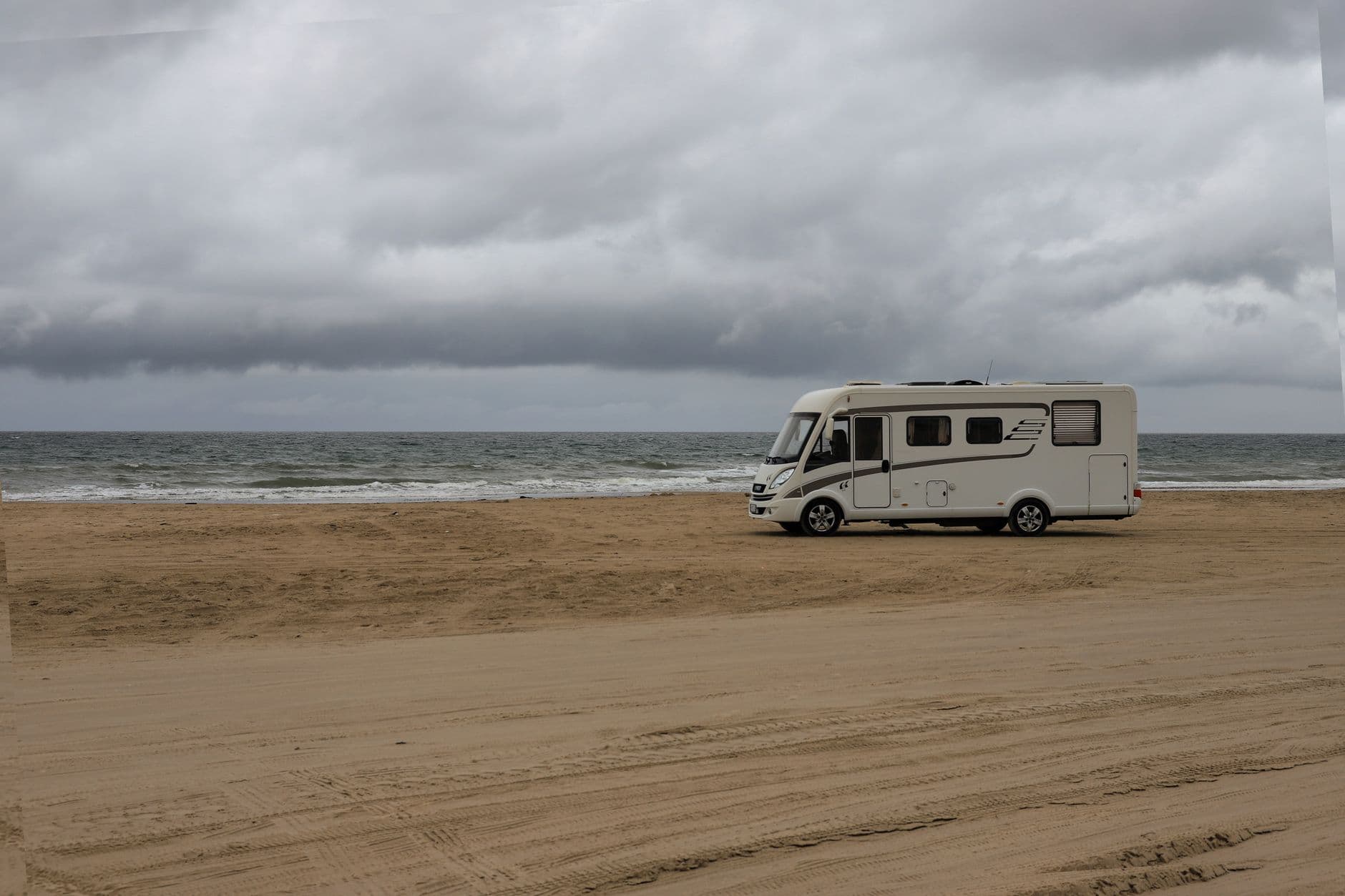 Witte integrale mobilhome op een zandstrand aan zee onder een grijze wolkenlucht