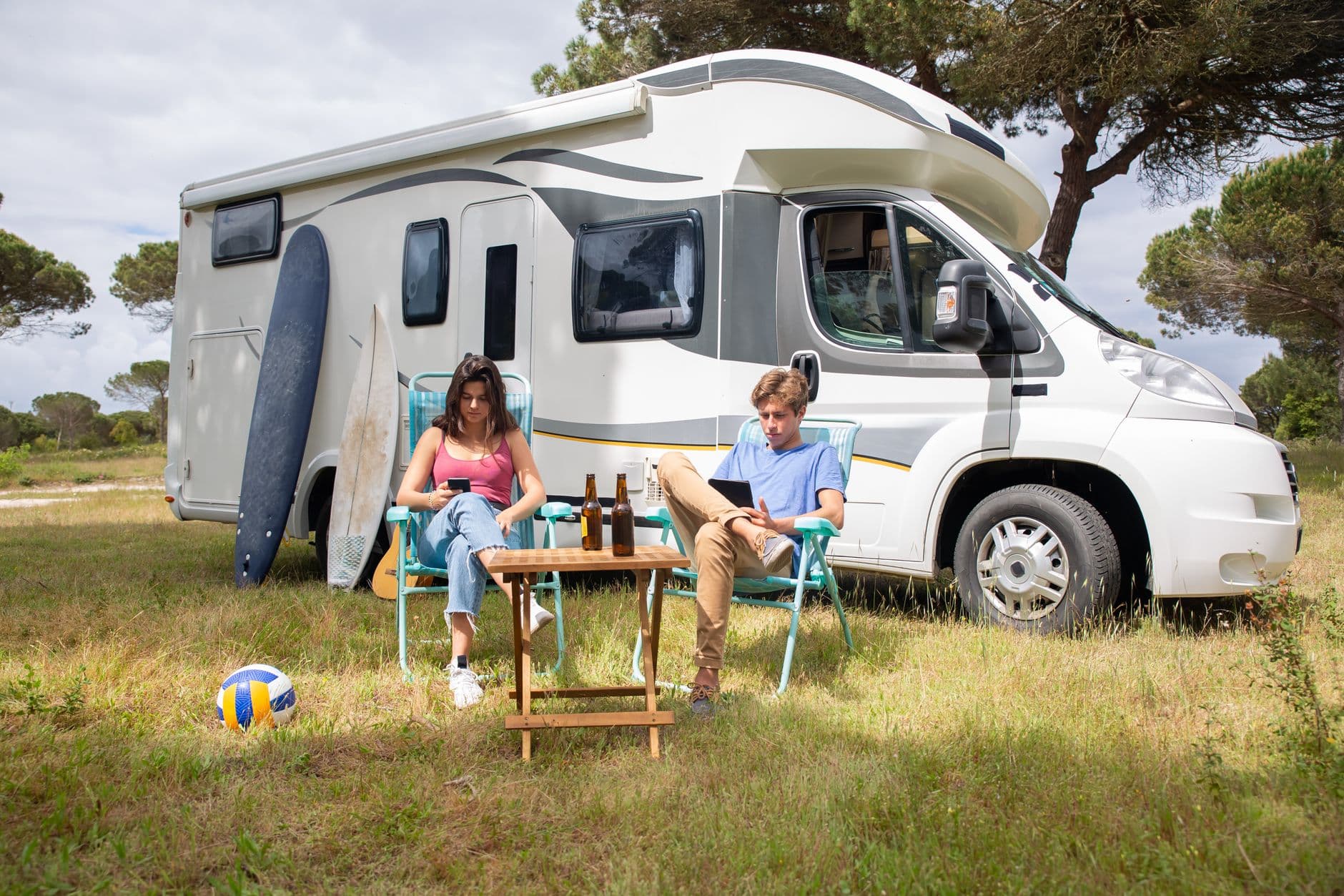 Witte mobilhome op een grasveld met twee jongeren in klapstoelen ervoor